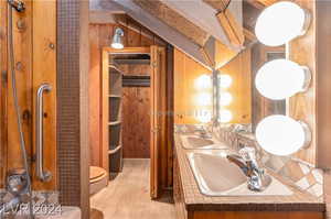 Bathroom featuring double vanity, backsplash, wood walls, toilet, and hardwood / wood-style floors