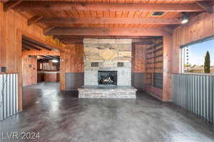 Unfurnished living room featuring wood ceiling, beam ceiling, wooden walls, and a stone fireplace