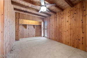 Carpeted spare room with wooden walls, ceiling fan, lofted ceiling with beams, and wood ceiling