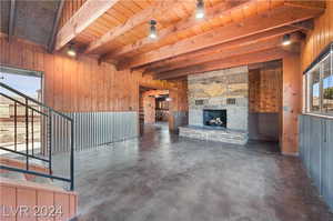 Unfurnished living room with a stone fireplace, beam ceiling, and wooden walls