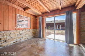 Empty room with wooden walls, beam ceiling, concrete flooring, and wood ceiling