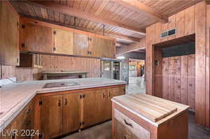 Kitchen featuring beamed ceiling, black electric cooktop, wood ceiling, wooden walls, and tile countertops