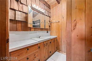 Bathroom featuring wood walls, vanity with extensive cabinet space, tasteful backsplash, and tile floors