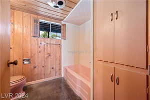 Bathroom with concrete flooring, wood ceiling, wooden walls, lofted ceiling, and toilet