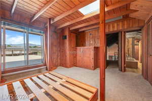 Unfurnished bedroom featuring wooden walls, vaulted ceiling with skylight, carpet, and wooden ceiling