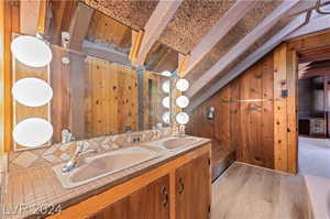 Bathroom with lofted ceiling with beams, hardwood / wood-style flooring, wooden walls, vanity with extensive cabinet space, and dual sinks