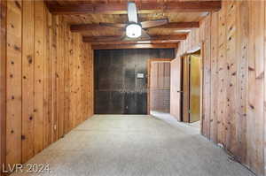 Empty room with beam ceiling, carpet flooring, ceiling fan, and wood walls