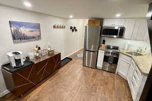 Kitchen with white cabinets, appliances with stainless steel finishes, light hardwood / wood-style floors, and backsplash