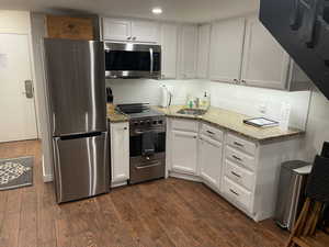 Kitchen featuring white cabinetry, appliances with stainless steel finishes, dark hardwood / wood-style flooring, and backsplash