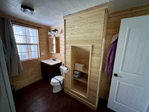 Bathroom featuring toilet, hardwood / wood-style floors, wooden walls, vanity, and a textured ceiling