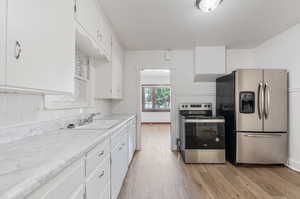 Kitchen featuring appliances with stainless steel finishes, white cabinets, tasteful backsplash, and light wood-type flooring