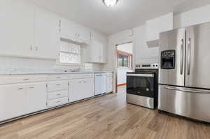 Kitchen with stainless steel appliances, light hardwood / wood-style flooring, white cabinets, and tasteful backsplash