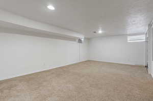 Basement featuring a textured ceiling, carpet flooring, and a wall unit AC