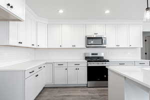 Kitchen featuring appliances with stainless steel finishes, hanging light fixtures, light hardwood / wood-style flooring, and white cabinetry