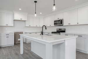 Kitchen with light hardwood / wood-style flooring, stainless steel appliances, a center island with sink, pendant lighting, and white cabinetry