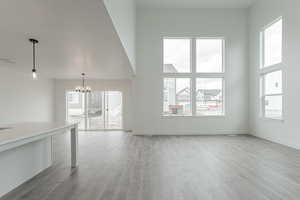 Unfurnished living room featuring a notable chandelier, hardwood / wood-style flooring, a towering ceiling, and plenty of natural light