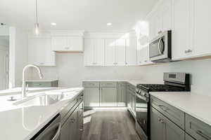 Kitchen featuring sink, appliances with stainless steel finishes, decorative light fixtures, and white cabinetry