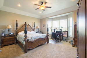 Carpeted bedroom featuring a raised ceiling and ceiling fan