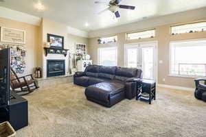 Carpeted living room with a wealth of natural light, a tiled fireplace, ceiling fan, and french doors