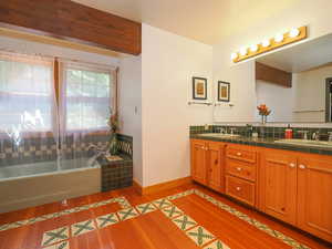 Lavish primary suite bath with tub, shower, double vanity and warm wood floors