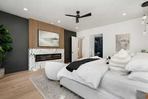 Bedroom featuring ceiling fan, light wood-type flooring, and a fireplace