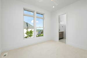 Interior space featuring ceiling fan, ensuite bathroom, and light carpet