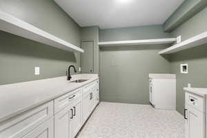 Clothes washing area with cabinets, sink, light tile floors, and washer hookup