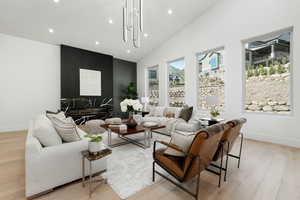 Living room with hardwood floor, vaulted ceilings, ample windows, and contemporary light fixture.