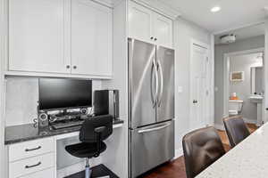 Kitchen with white cabinetry, dark wood-type flooring, dark stone counters, stainless steel refrigerator, and tasteful backsplash