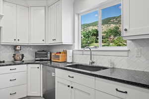 Kitchen featuring dark stone counters, a healthy amount of sunlight, white cabinets, and tasteful backsplash