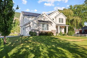 View of front of property with a front lawn, a garage, and solar panels