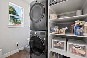 Laundry room featuring stacked washing maching and dryer and dark tile flooring