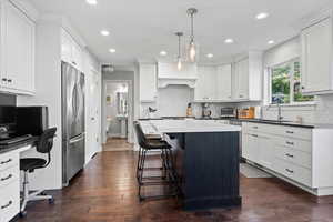 Kitchen featuring stainless steel refrigerator, white cabinetry, a center island, dark wood-type flooring, and sink