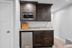 Bar with dark brown cabinetry, light stone countertops, stainless steel appliances, and light colored carpet