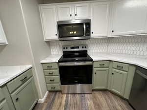 Kitchen featuring white cabinets, decorative backsplash, stainless steel appliances, and dark wood-type flooring