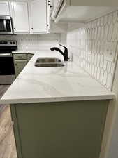 Kitchen with white cabinetry, sink, light stone counters, appliances with stainless steel finishes, and green cabinetry