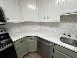 Kitchen featuring green cabinets, sink, light stone countertops, and stainless steel appliances