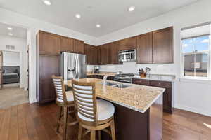 Kitchen with a kitchen breakfast bar, stainless steel appliances, dark wood-type flooring, light stone counters, and a kitchen island with sink