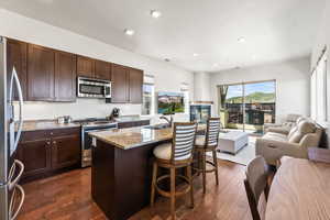 Kitchen featuring stainless steel appliances, a kitchen island with sink, a kitchen bar, dark wood-type flooring, and sink