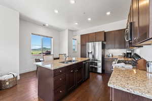 Kitchen featuring dark hardwood / wood-style floors, a center island with sink, stainless steel appliances, light stone counters, and sink