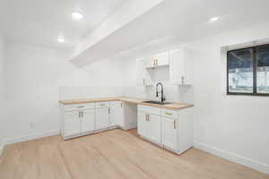 Kitchen featuring white cabinets, sink, backsplash, and light hardwood / wood-style flooring