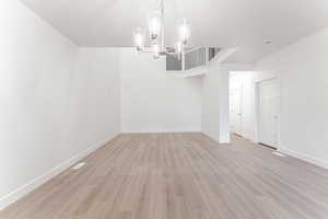 Empty room with a notable chandelier and light wood-type flooring