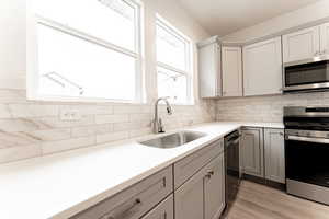 Kitchen featuring appliances with stainless steel finishes, sink, light hardwood / wood-style floors, gray cabinets, and decorative backsplash