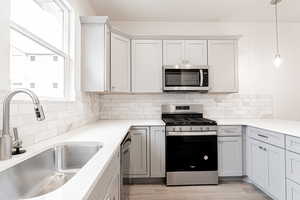 Kitchen with backsplash, sink, decorative light fixtures, light wood-type flooring, and appliances with stainless steel finishes