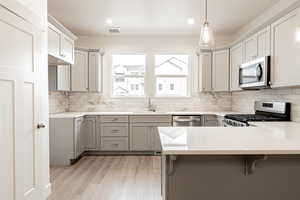 Kitchen featuring appliances with stainless steel finishes, sink, light wood-type flooring, kitchen peninsula, and hanging light fixtures