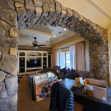 Stone arch detail in carpeted living room with fireplace, floating ceiling with ceiling fan.