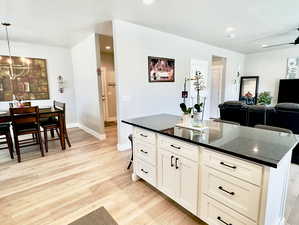 Kitchen with light hardwood / wood-style floors, decorative light fixtures, an inviting chandelier, a kitchen island, and white cabinetry