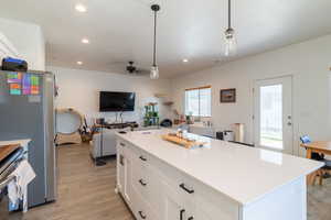 Kitchen with a kitchen island, white cabinetry,  light LVP flooring, and decorative light fixtures