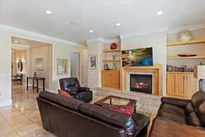 Tiled living room featuring built in features, ornamental molding, and a fireplace