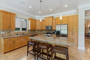 Kitchen with a kitchen island, stainless steel appliances, decorative light fixtures, backsplash, and sink